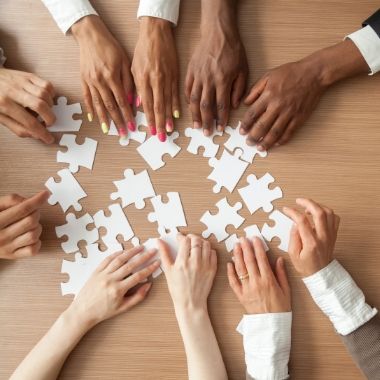 Group of Hands Solving Puzzle on a Table.